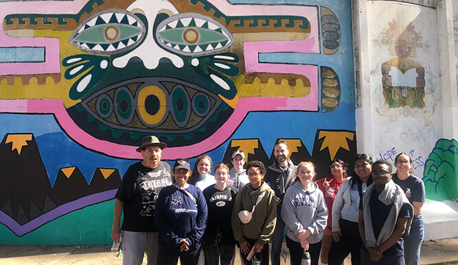 A group of students stands outdoors in front of a cultural mural in San Diego.