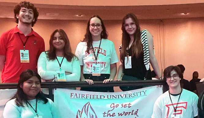 Fairfield students posing with a 'Go Set the World on Fire!' Campus Ministry banner at an annual Ignatian gathering.