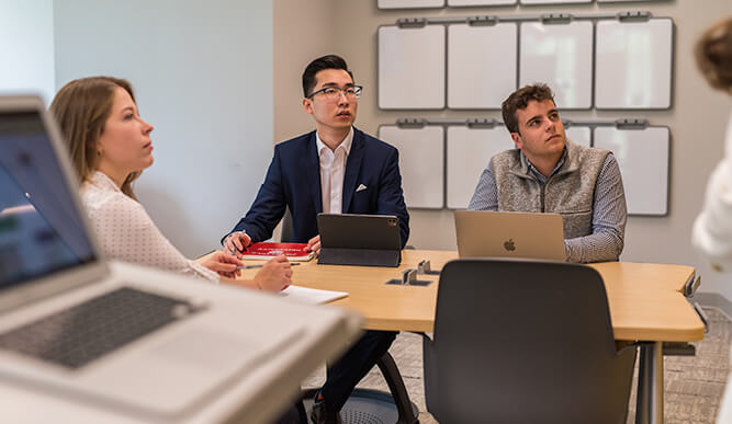 Three individuals seated at a table, each using a laptop, engaged in a collaborative work session.
