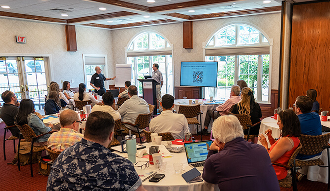 A diverse group of people sitting at tables in a room, interacting and sharing ideas in a collaborative environment.