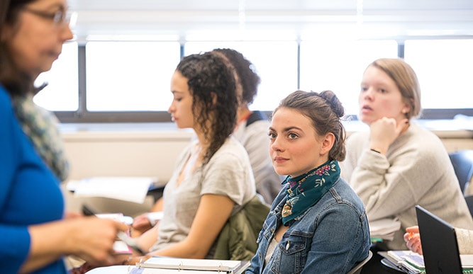 Female students listening to a lecture in a classroom setting.