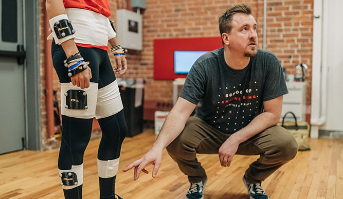 Professor John Drazan pointing to and explaining a piece of equipment on a student, which monitors her movement.