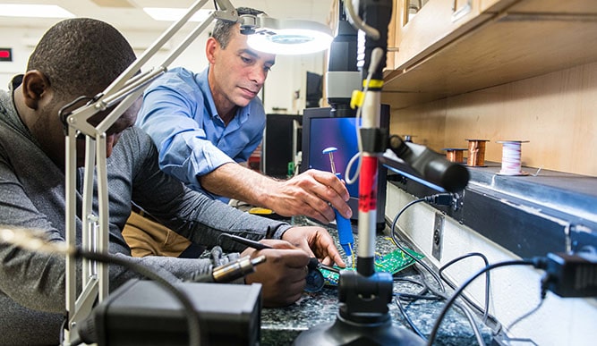 Professor James Cavallo working together on adjusting a circuitboard.