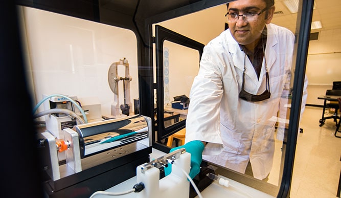 Professor Isaac Macwan inspecting a piece of 3D printed material in the printer.