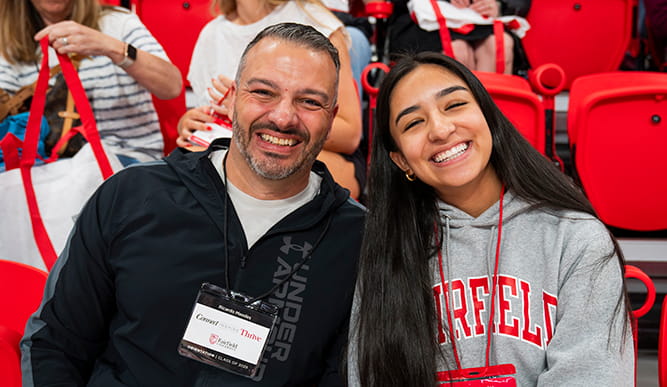 A Fairfield University student and family member smile together during New Student Orientation while seated in an arena.