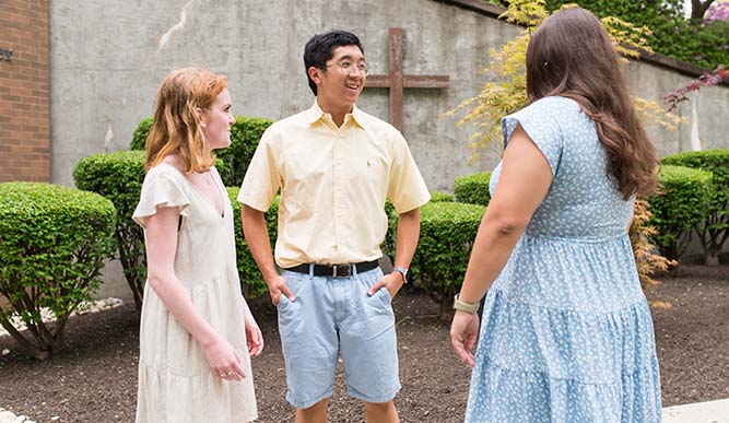 Three people engaged in conversation outside a church, with the building's architecture visible in the background.