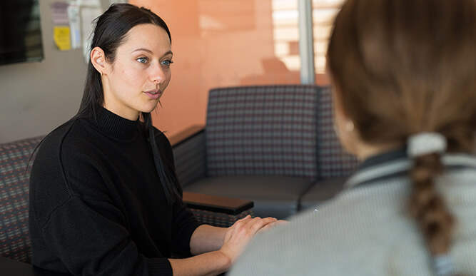 Two women converse in a bright office waiting area; one listens attentively while the other gestures, creating a calm, professional tone.