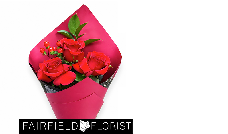 A bouquet of three vibrant red roses wrapped in deep pink paper, accented with green leaves and small red berries, conveying a romantic tone.