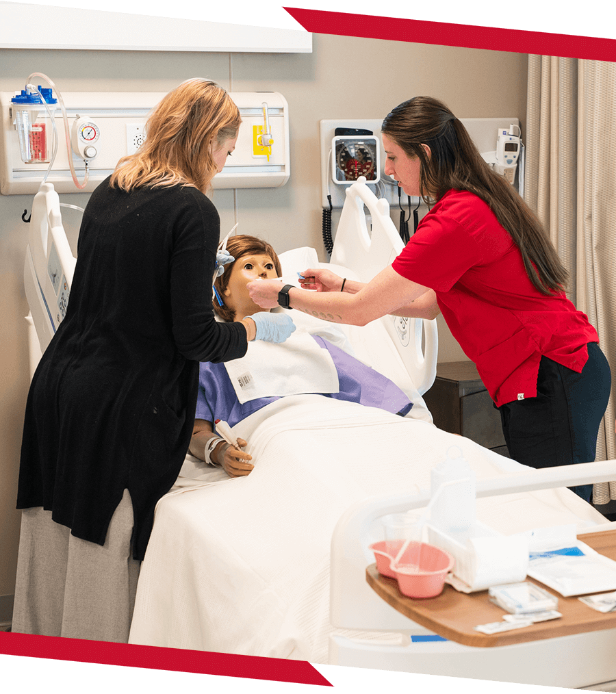 Student wearing red scrubs practicing on a fake patient in a nursing class.