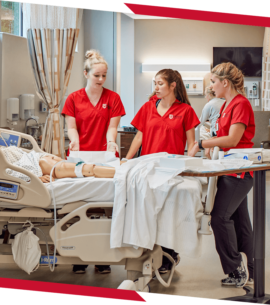 Three students in a classroom that resembles a hospital learning nursing skills.