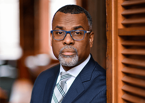 Eddie S. Glaude, Jr. wearing glasses and a formal suit, standing confidently with a neutral expression.