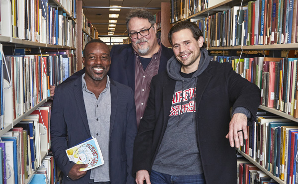 Three men standing in between book aisles at the library. 
