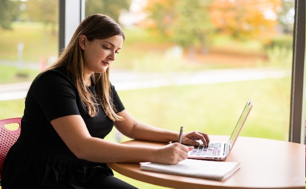 Photo of student sitting at table typing on laptop computer.