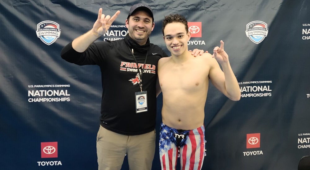 Men's Swimming and Diving student-athlete posing with his coach in front of a National Championships backdrop.