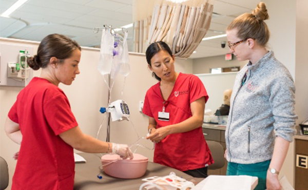 Student nurses performing a mock IV procedure in a simulation lab.