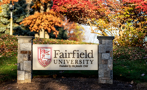 Sign at Fairfield University entrance with fall foliage in background.