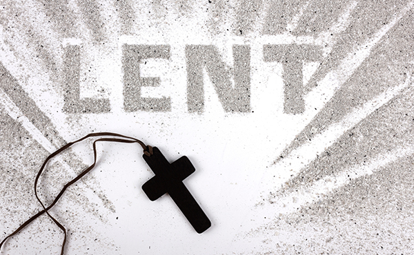 The letters 'Lent' spelled out in ashes next to a dark colored cross.
