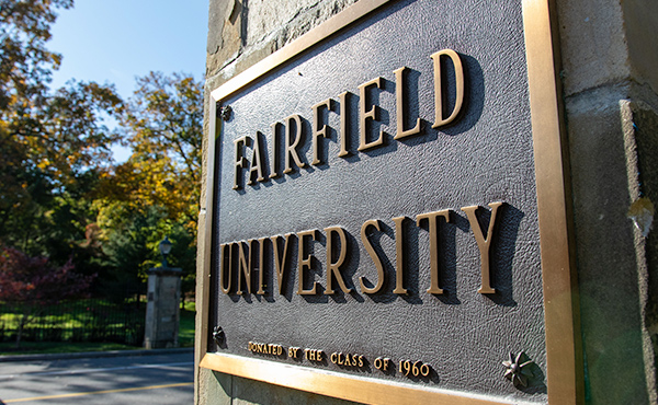 Close-up photo of a dark commemorative plaque on building with Fairfield University written on it.