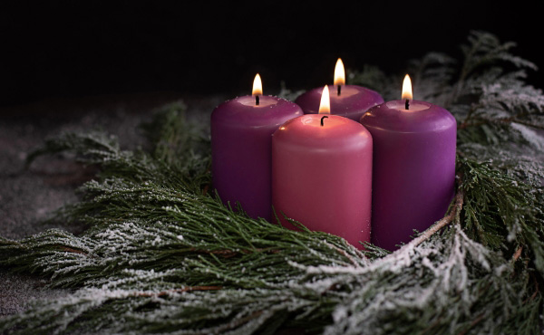 Four purple lit candles sitting inside a green wreath. 