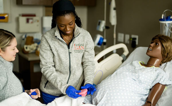 Two female nursing students simulating a midwifery scenario with a simulation doll.