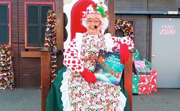 A women dressed as Mrs. Claus sitting in a chair holding a book.