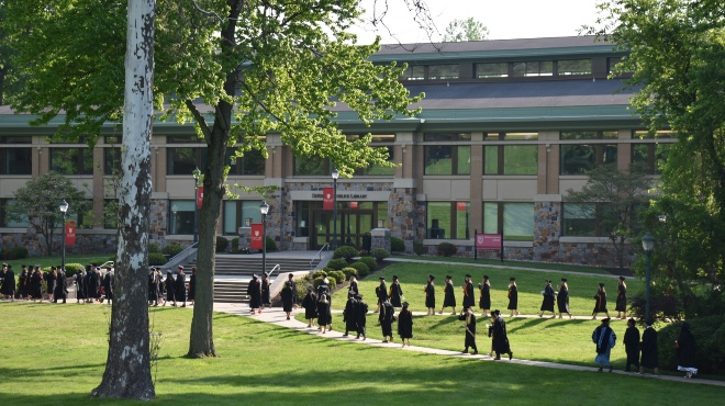 A line of graduating students walking through campus in their cap and gown